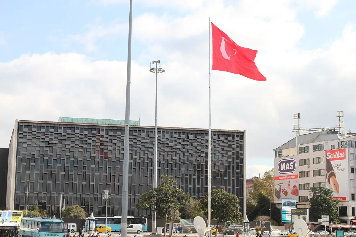 A fachada escura com padrão de grelha do Centro Cultural Atatürk, junto a altos mastros com uma grande bandeira turca